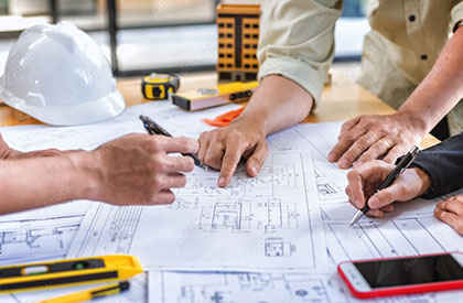 Work table with construction hat, phone, blueprints and peoples arms on table